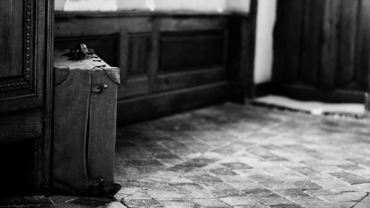 A business traveler smiling next to his sleek metal-framed hardshell suitcase outside an airport terminal.